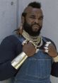 Mr. T showcases his iconic style with a mohawk, gold chains, and denim overalls, embodying his tough persona from The A-Team.