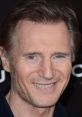 Liam Neeson smiles while attending a premiere, showcasing his signature charm and captivating blue eyes.