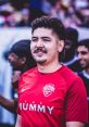 YouTuber smiling in a red soccer jersey at a lively event, showcasing a fun spirit and engaging community atmosphere.