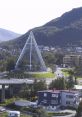 Modern glass pyramid building in Norway, surrounded by trees and buildings, with mountains in the backdrop.