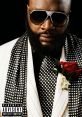 Rick Ross exudes style in a sharp polka dot suit with sunglasses and a red rose, showcasing his iconic fashion sense.