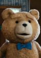 Ted, the beloved stuffed bear, sporting a blue bow tie with a charming expression in a cozy interior setting.