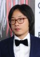 Jian Yang attending a formal event, wearing a black bow tie and suit, with a focused expression against a colorful backdrop.