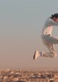 Man in stylish outfit jumps over a city skyline at sunset, symbolizing freedom and aspiration.