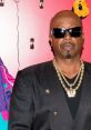 MC Hammer poses confidently in a stylish black outfit with gold chains, showcasing his iconic hip-hop style.