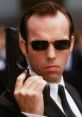 Agent Smith holding a gun in sunglasses, embodying an iconic prank call character. Perfect for "Prank Call Clips: Agent Smith.