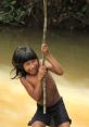 Awa child joyfully swinging on a stick over a river, showcasing traditional play and cultural heritage in nature.