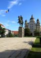 Statue of a rider on horseback in Targu, with the Romanian flag and a historic building in the background.