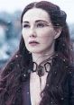 Melisandre from Game of Thrones stands in the snow, her long red hair flowing, embodying mystery and power.