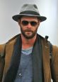 Stylishly dressed man with a beard in a gray hat and sunglasses, showcasing a modern, urban fashion aesthetic.