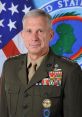 U.S. military leader in uniform, adorned with medals, standing against an American flag backdrop, representing command authority.