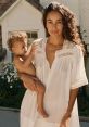 Mom holding a baby in a casual white dress, exuding warmth and tenderness in a serene outdoor setting.