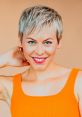 Smiling woman with short, blonde hair wearing an orange top, showcasing vibrant blue eyes against a warm background.