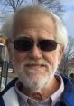 Smiling elderly man with white beard and sunglasses, reminiscent of online personality Angry Grandpa, outdoors in a park.