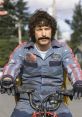 Character in Hot Rod Movie wears a jumpsuit with a mustache, riding a bike against a scenic backdrop. Fun and quirky vibe.