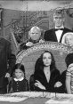 The Addams Family cast in a classic black-and-white scene, featuring Morticia, Gomez, and their unique children.