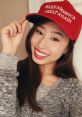 Kathy Zhu smiles and poses with a red "Make America Great Again" cap, showcasing her support for the campaign.