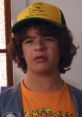 Dustin Henderson wearing a yellow camp hat and orange T-shirt, showcasing his signature quirky style in "Stranger Things.