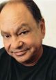 Cheech Marin smiling, known for his comedic style and contributions to film and music, wearing a black shirt.