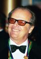 Jack Nicholson smiling broadly, wearing sunglasses and a tuxedo, with colorful ribbons at a prestigious event.