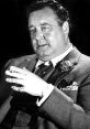 Jackie Gleason gestures expressively in a classic black and white portrait, showcasing his iconic style and charisma.