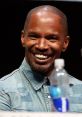 Jamie Foxx smiling at a panel event, wearing a denim shirt, with a water bottle visible in the foreground.