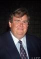 John Candy smiling in a suit, showcasing his charismatic personality and comedic charm at a public event.