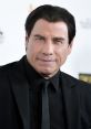 John Travolta smiling confidently in a black suit, showcasing his timeless style at a red carpet event.