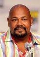 Kevin Michael Richardson speaking at a panel, showcasing his vibrant shirt and distinctive charisma at a popular convention.