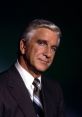 Leslie Nielsen in a sharp suit, exuding charisma and confidence, set against a dark gradient background.