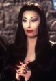 Morticia Addams with long black hair, red lips, and striking nails, exuding a glamorous gothic elegance.