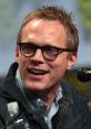 Paul Bettany smiling at a panel discussion, wearing glasses and a denim jacket, showcasing his engaging personality.