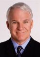 Steve Martin smiling in a dark suit with a blue shirt, showcasing his signature hairstyle and warm charisma.