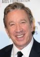 Tim Allen smiling at an event, showcasing his signature charisma and style in a classic suit and tie.