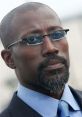 Wesley Snipes in a formal suit, showcasing a confident expression and stylish glasses, embodying charisma and professionalism.