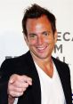 Will Arnett smiling and pointing directly at the camera, dressed in a black blazer and white shirt at a film festival event.