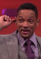 Will Smith playfully gestures during an interview, showcasing his stylish outfit and engaging personality.