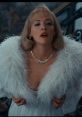 Debbie Jellinsky in glamorous white attire with a feathered wrap and pearl necklace, exuding elegance and allure.