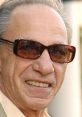 Henry Hill, infamous mobster, sporting sunglasses, smiles confidently, reflecting his notorious lifestyle in organized crime.