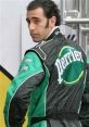 Jean Girard in a green racing suit with Perrier branding, showcasing his confident demeanor at the racetrack.