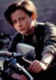 Young boy with short hair, gazing thoughtfully while sitting on a motorcycle, embodying the spirit of John Connor.