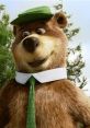 Yogi Bear, wearing a green hat and tie, smiles playfully in a forested backdrop. A beloved cartoon character.