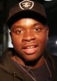 Big Shaq smiles while wearing a black cap and hoodie, reflecting his vibrant personality and unique style.