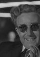 Dr. Strangelove character with glasses smiling, embodying dark comedy and satire of the nuclear age in classic film.