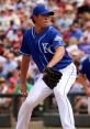 Pitcher in a blue Kansas City Royals uniform prepares to throw a pitch during a baseball game with cheering fans in the background.