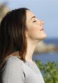 Woman practicing deep breathing outdoors, enjoying fresh air by the coast, promoting relaxation and mindfulness.