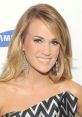 Carrie Underwood smiles radiantly in a stylish black and white outfit, showcasing her glamorous earrings at a celebrity event.