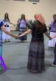 Women engaged in a joyful circle dance, wearing colorful skirts and tops, showcasing community and rhythm in motion.