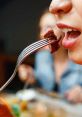 Close-up of a person about to eat a piece of meat on a fork, enjoying a delicious meal with friends.