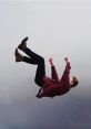 Young man in a flannel shirt appears to be falling against a muted gray background, capturing a moment of free fall.